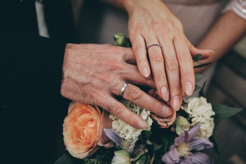 Closeup of the hands of a couple holding each other over a bouquet