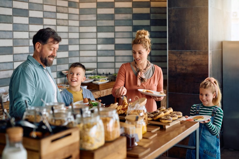 Happy parents and their kids enjoying in buffet breakfast in hotel.